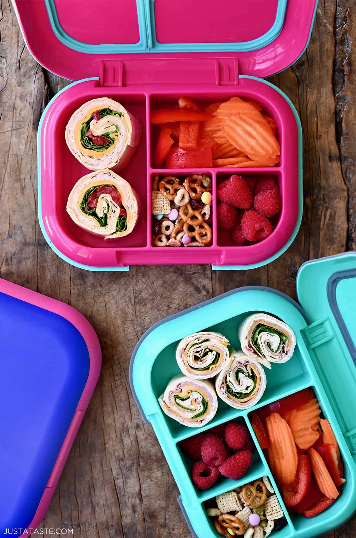 Two lunchboxes containing pinwheel sandwiches, fresh fruit and veggies, and trail mix.