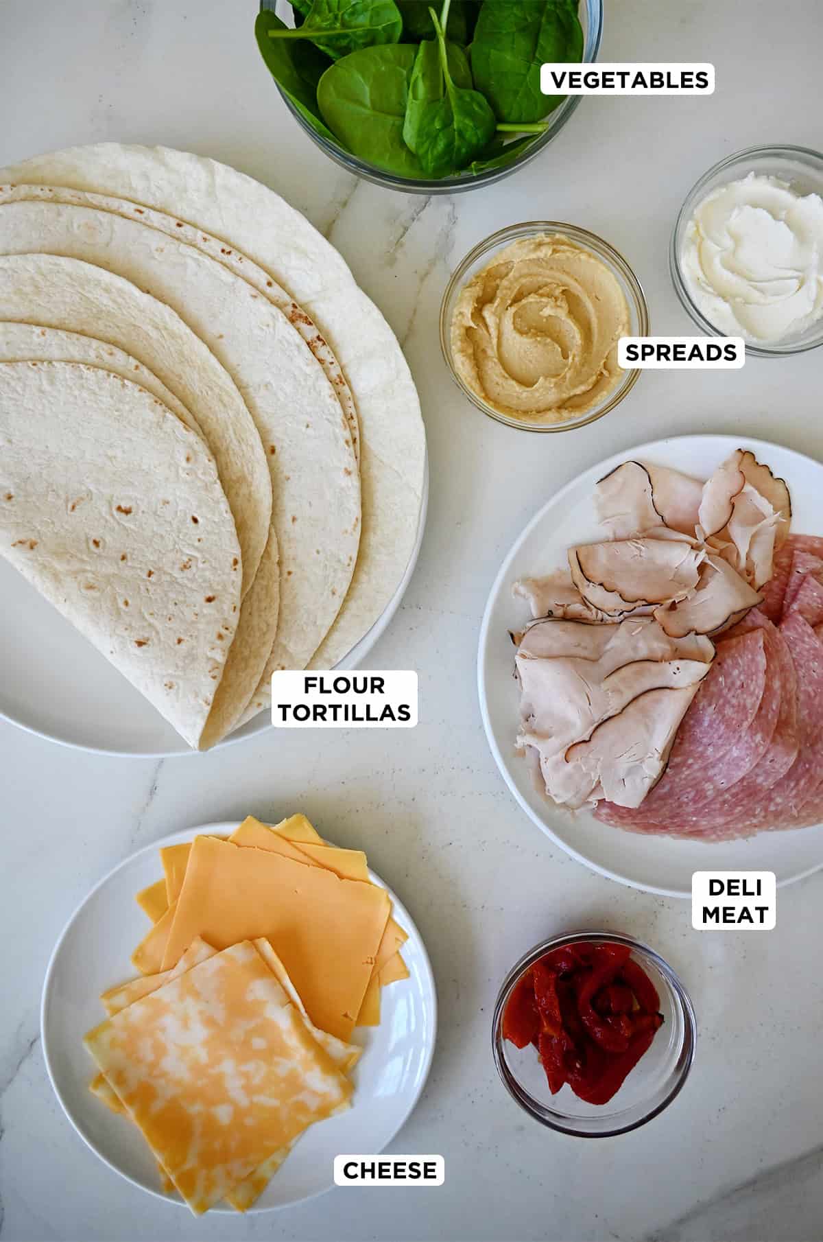 Ingredients to make pinwheel sandwiches, including flour tortillas, thinly sliced deli meat, slices of cheese, spinach, mayonnaise, mustard and roasted red peppers.