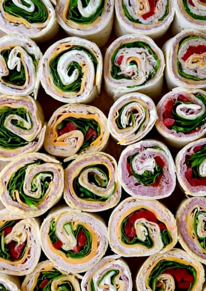 Several different flavors of pinwheel sandwiches, including ham and cheese pinwheels, turkey and spinach pinwheels, and salami pinwheel sandwiches.