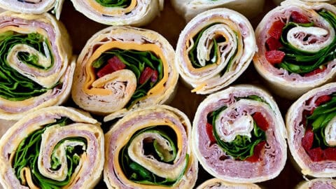 Several different flavors of pinwheel sandwiches, including ham and cheese pinwheels, turkey and spinach pinwheels, and salami pinwheel sandwiches.