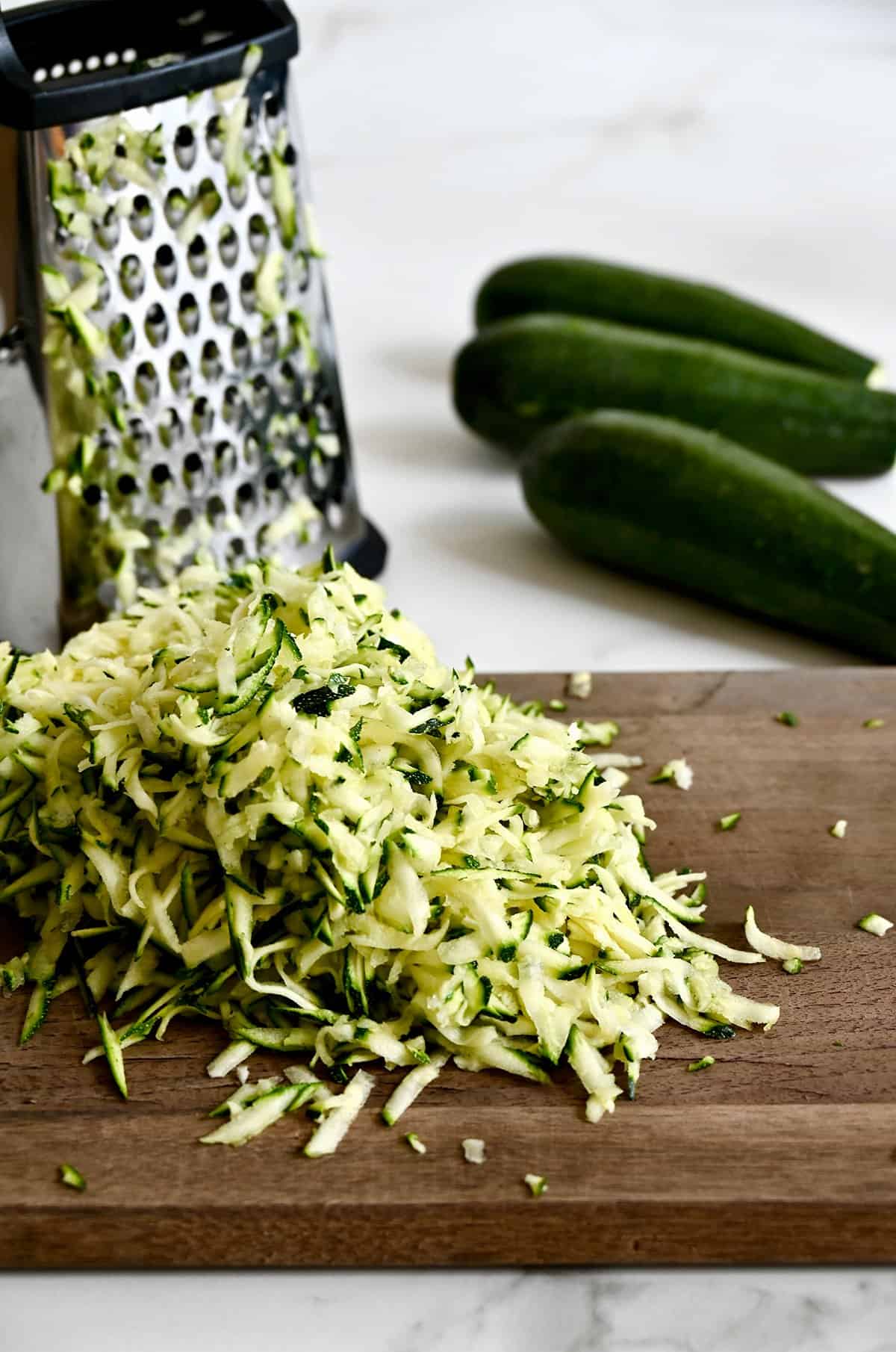 A pile of shredded zucchini on a cutting board next to a box grater.