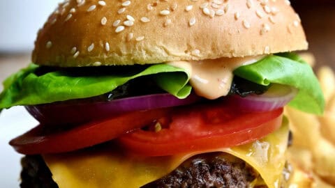 A homemade smash burger with double beef patties, a slice of cheddar cheese, tomatoes, lettuce and homemade burger sauce on a plate with French fries.