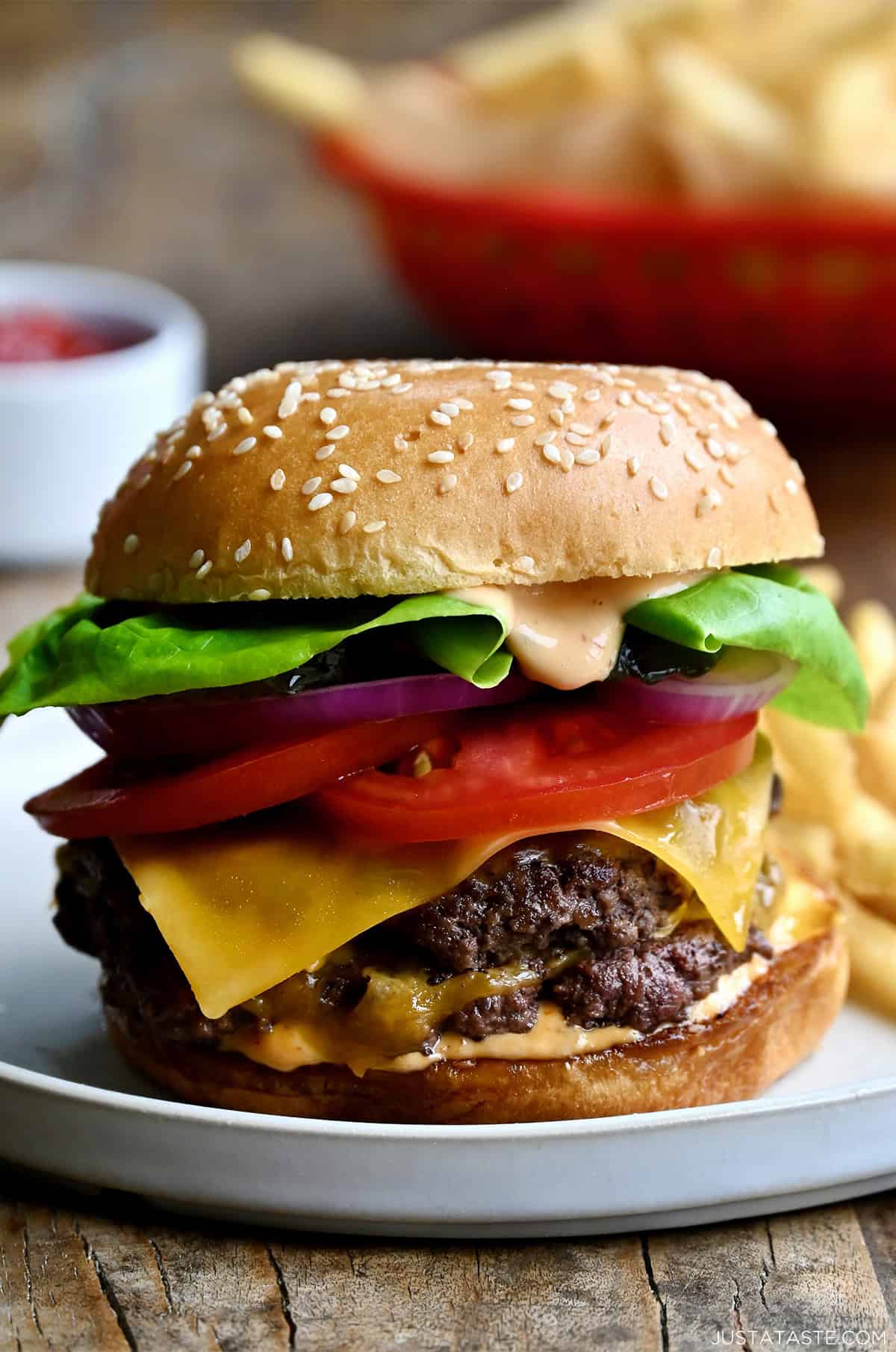 A homemade smash burger with double beef patties, a slice of cheddar cheese, tomatoes, lettuce and homemade burger sauce on a plate with French fries.