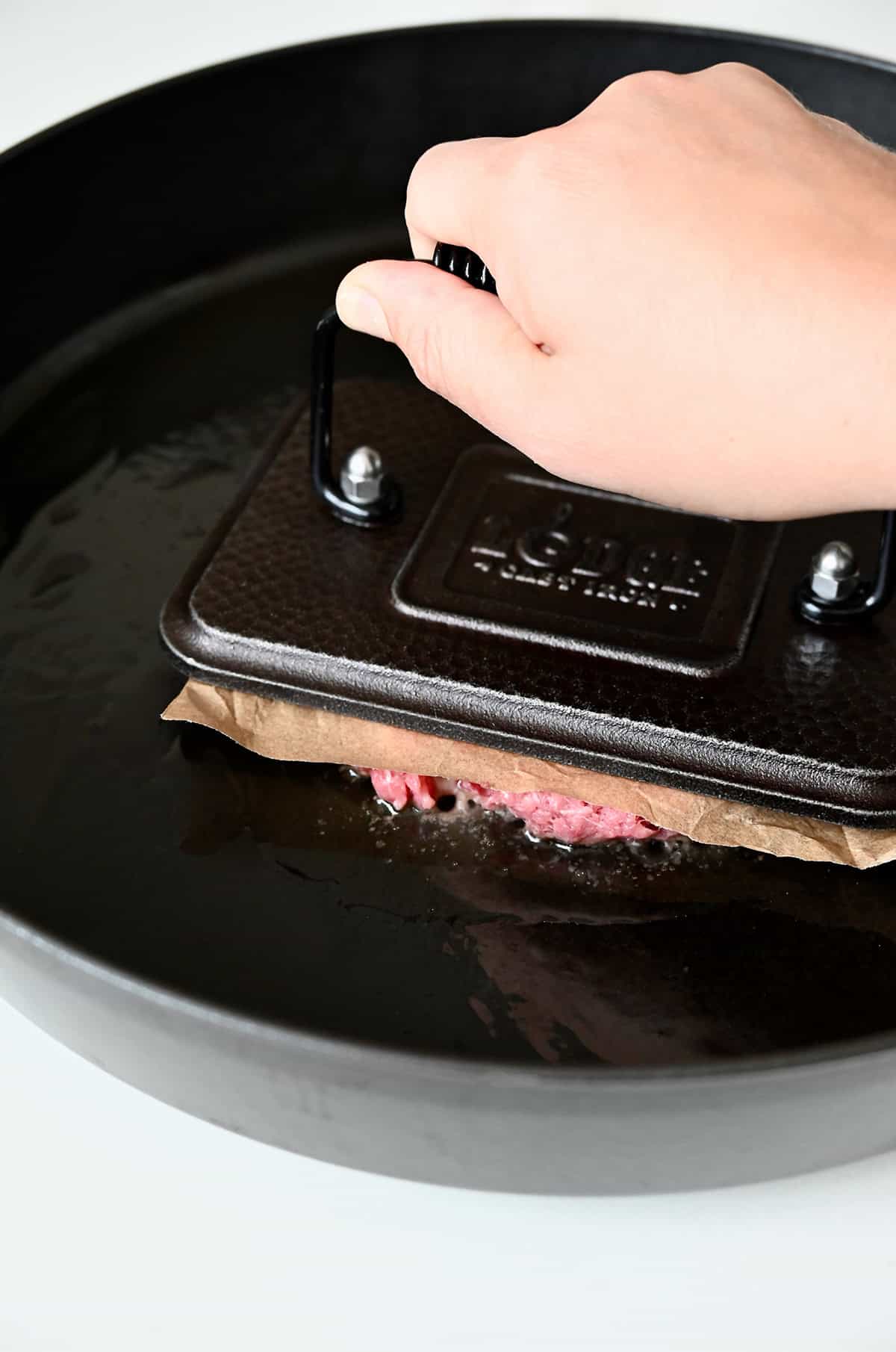 Smashing a burger patty in a hot skillet with a burger press.