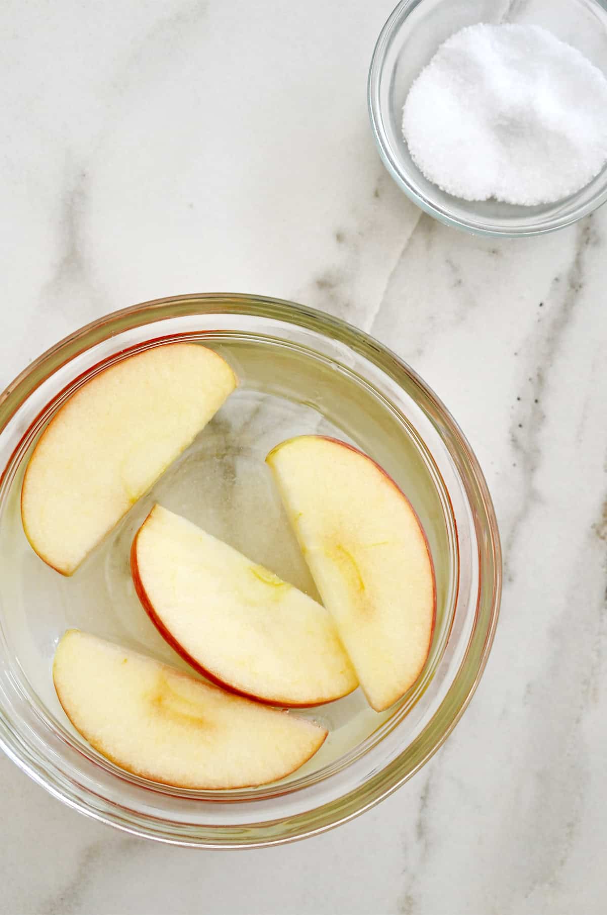 Four apple slices soaking in a saltwater bath in a small bowl.
