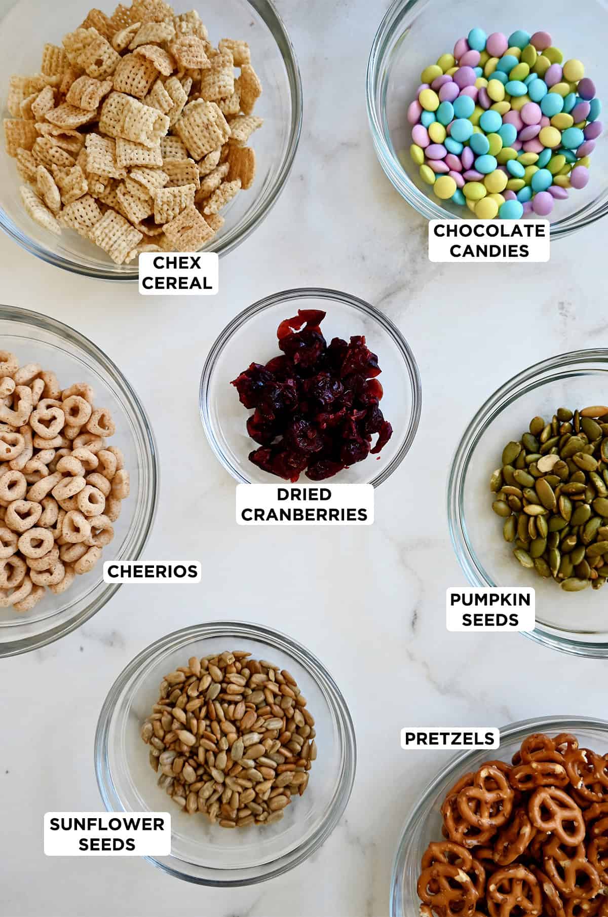 Ingredients to make a school-friendly trail mix: Cheerios, Chex Cereal, M&Ms, dried cranberries, pumpkin seeds, mini pretzels and sunflower seeds.