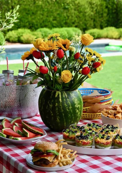 Watermelon centerpiece on a table lined with a red and white-checkered tablecloth.