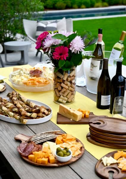 An outdoor table set with wine and cheese for hosting a small party with friends and family.