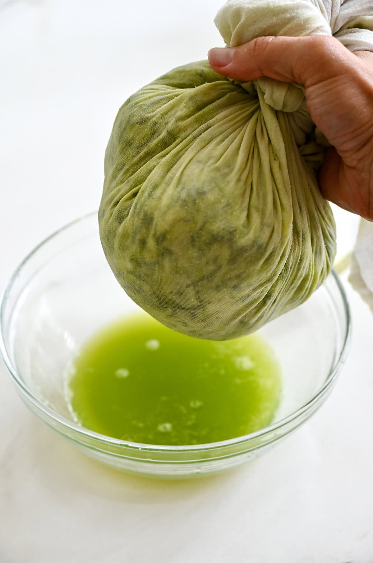 Squeezing out excess moisture from shredded zucchini in a cheese cloth over a bowl.