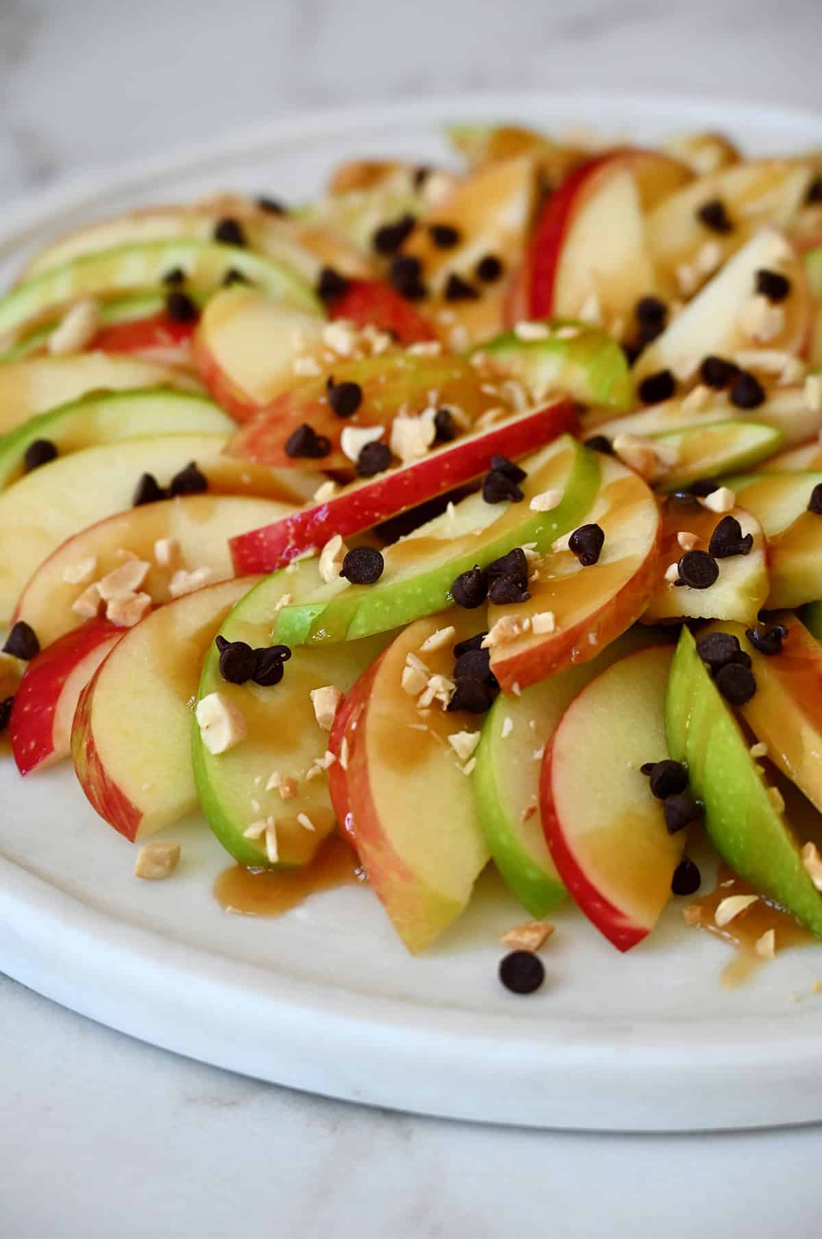 Apple nachos with caramel sauce, mini chocolate chips and crushed peanuts on a serving platter.