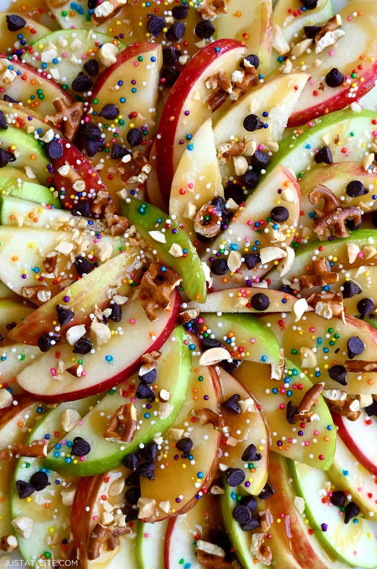 Apple nachos made with red and green apple slices topped with caramel drizzle, chocolate chips, chopped peanuts, sprinkles and pretzels.
