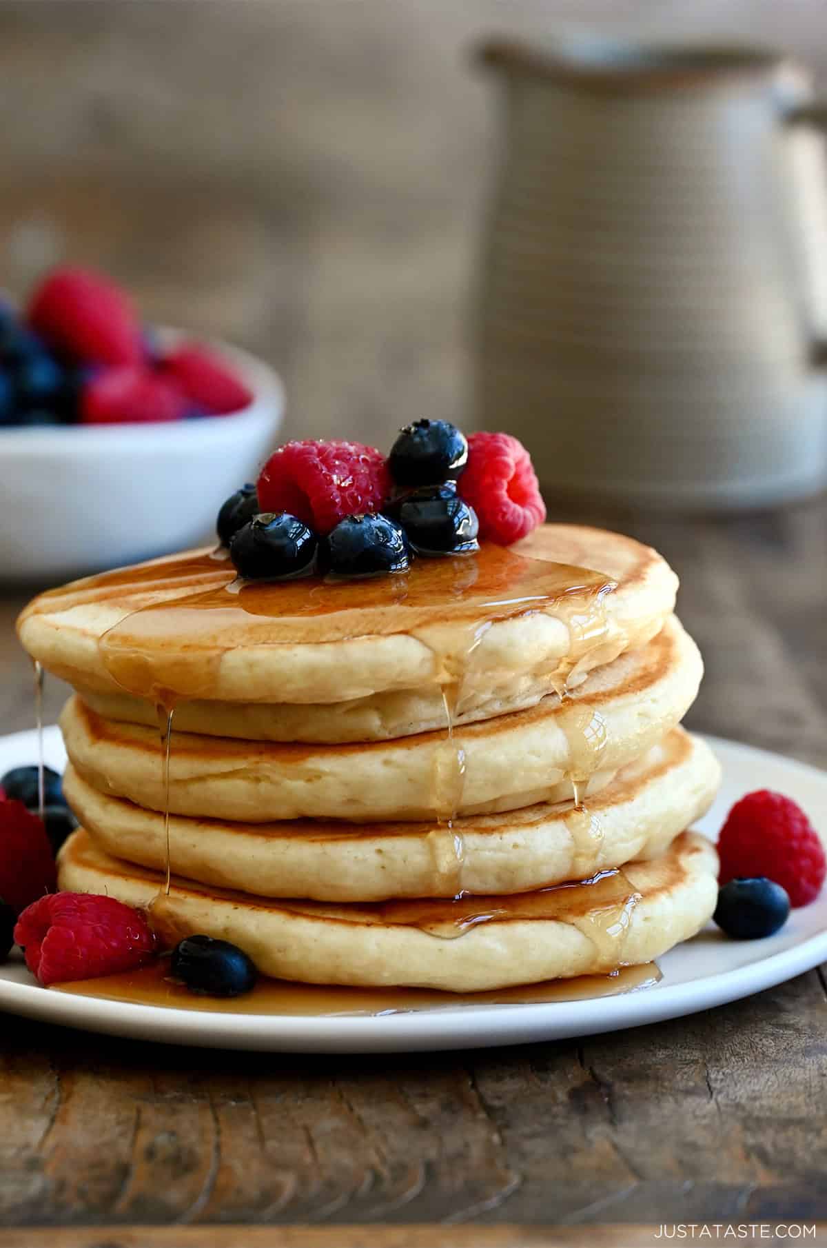 A stack of cottage cheese pancakes on a white plate topped with fruit and syrup being drizzled on top
