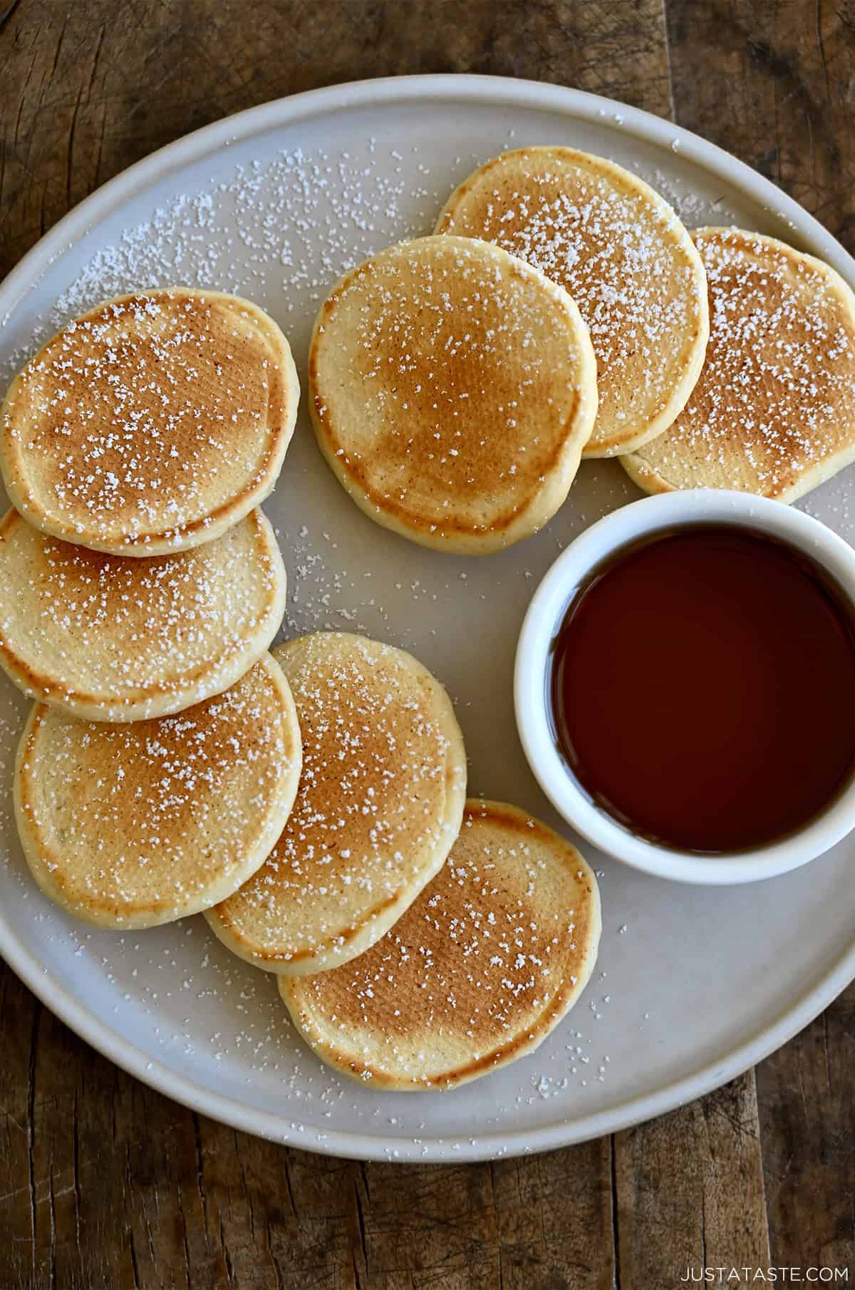 A plate containing silver dollar-sized pancakes dusted with powdered sugar and a small container of syrup