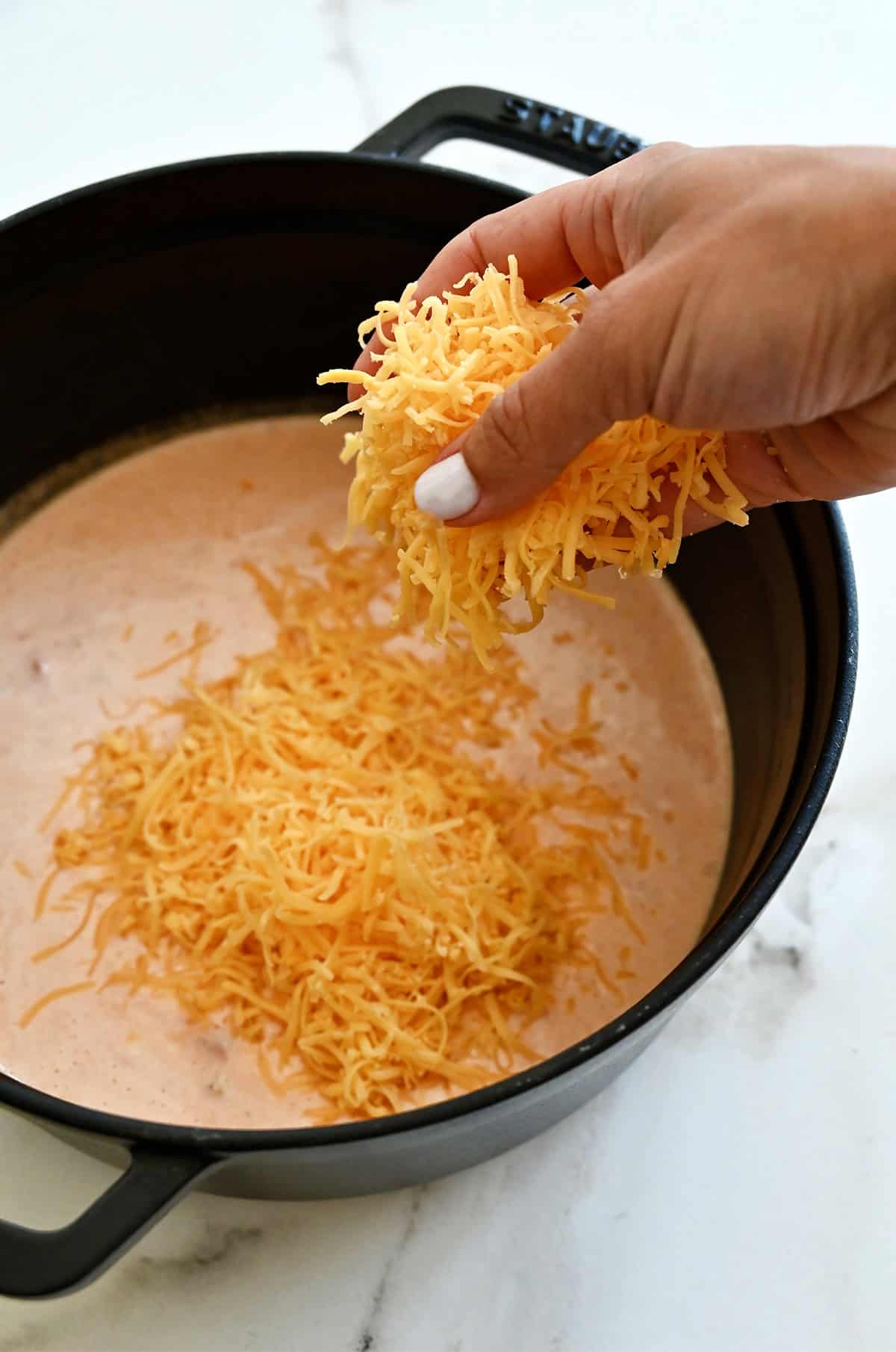 Shredded cheddar cheese is being added to a saucepan to make warm queso sauce.