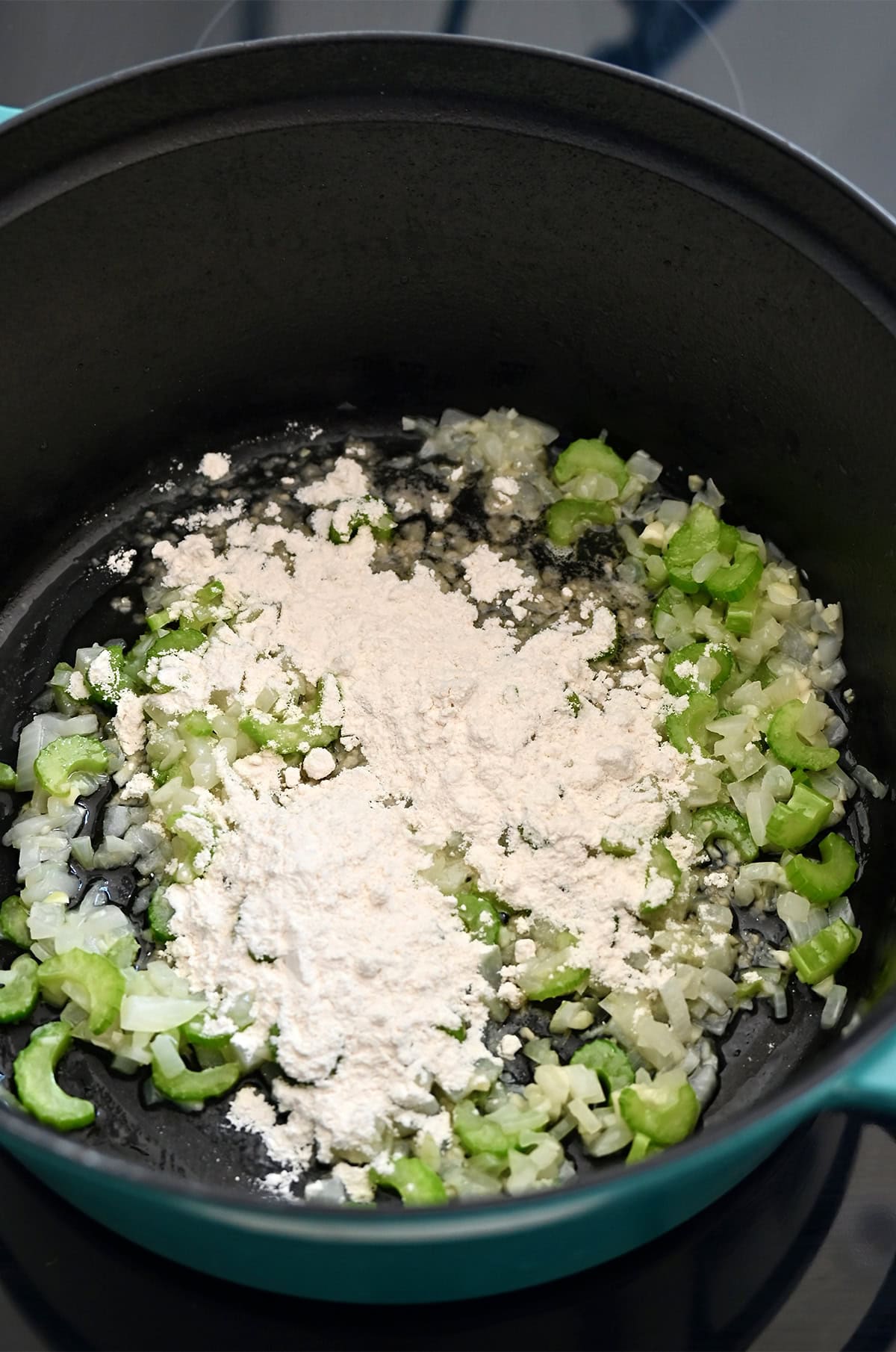 Step two in making broccoli soup: Adding flour to the stockpot with sautéed aromatics and butter to make a quick roux.