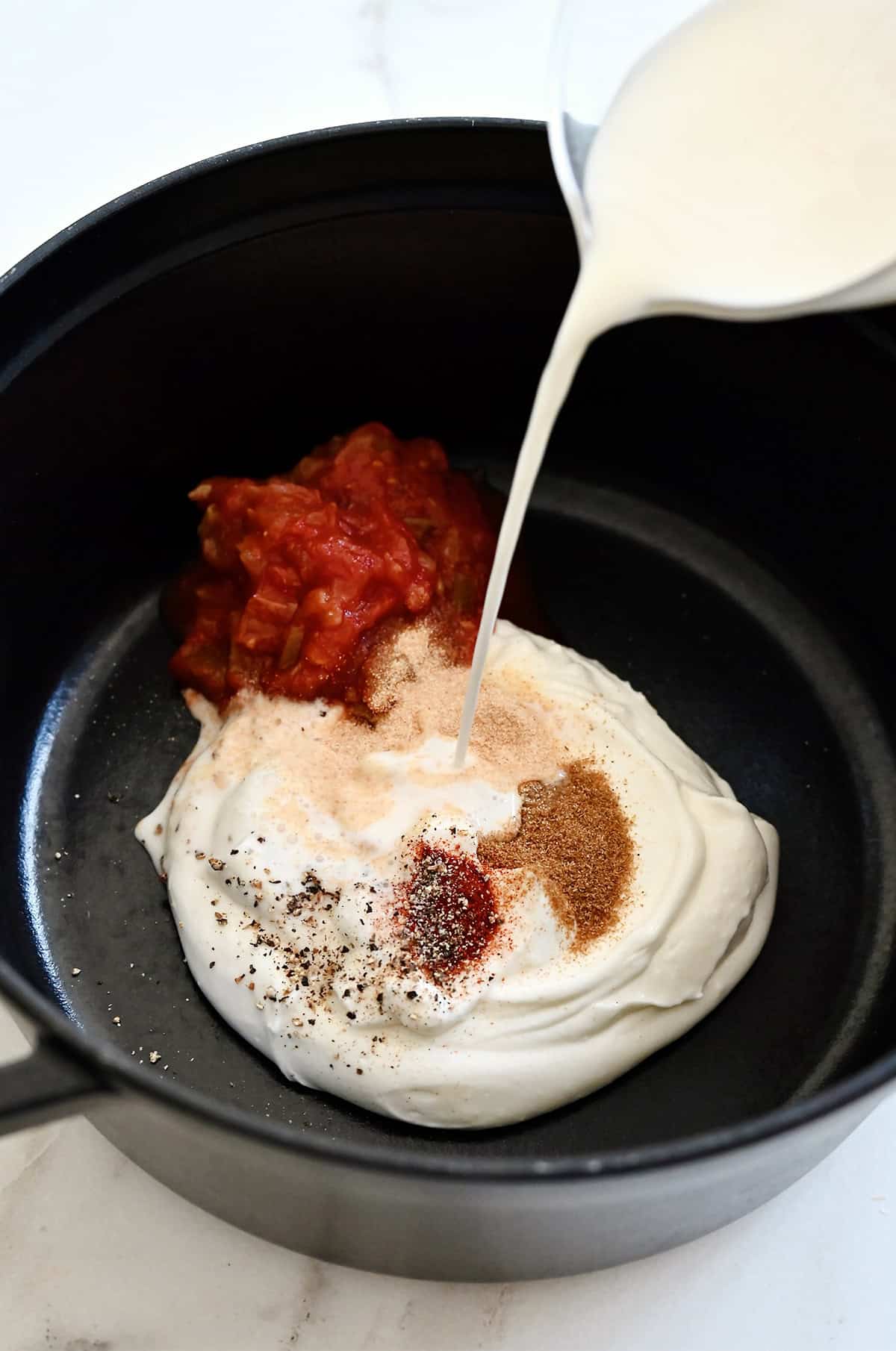 Milk being poured over blended cottage cheese, salsa and taco seasonings in a saucepan.