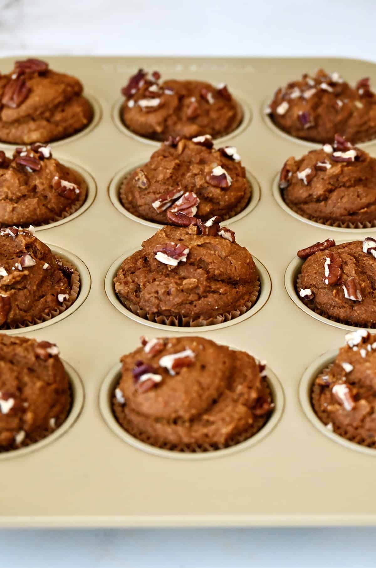 Freshly baked pumpkin muffins with pecans in a muffin tin.