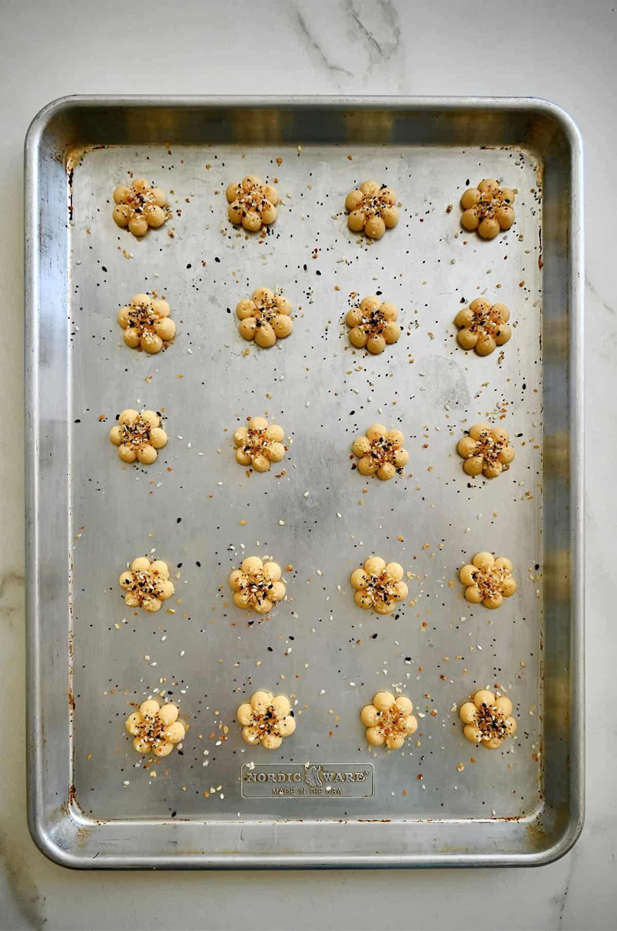 Baked cheddar spritz cookies with everything bagel seasoning on an unlined baking tray.