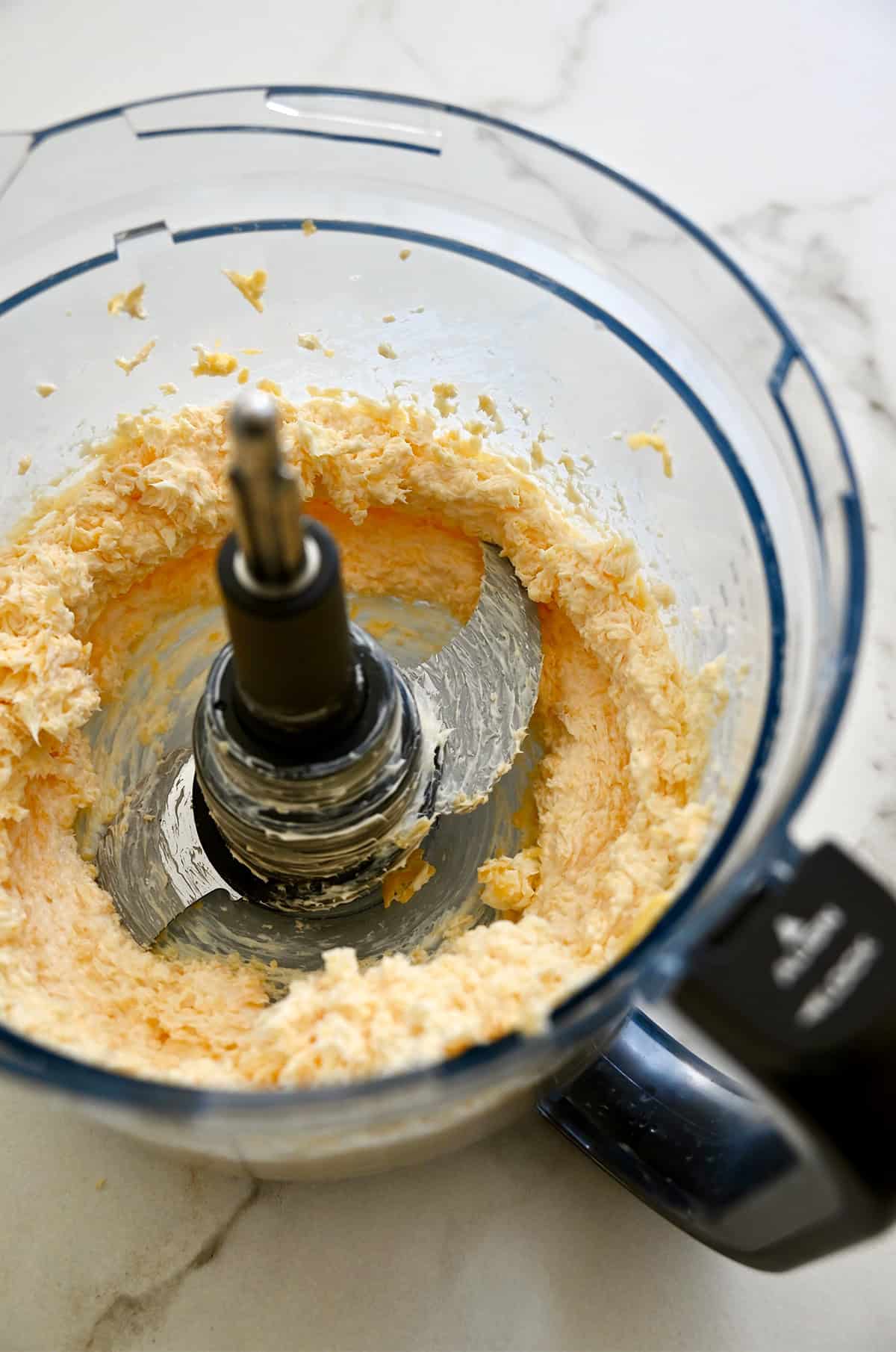Shredded cheddar cheese blended with butter in a food processor.