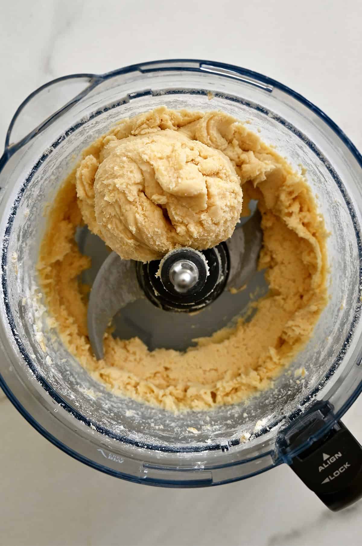 Cheese shortbread dough in a bowl of a food processor.
