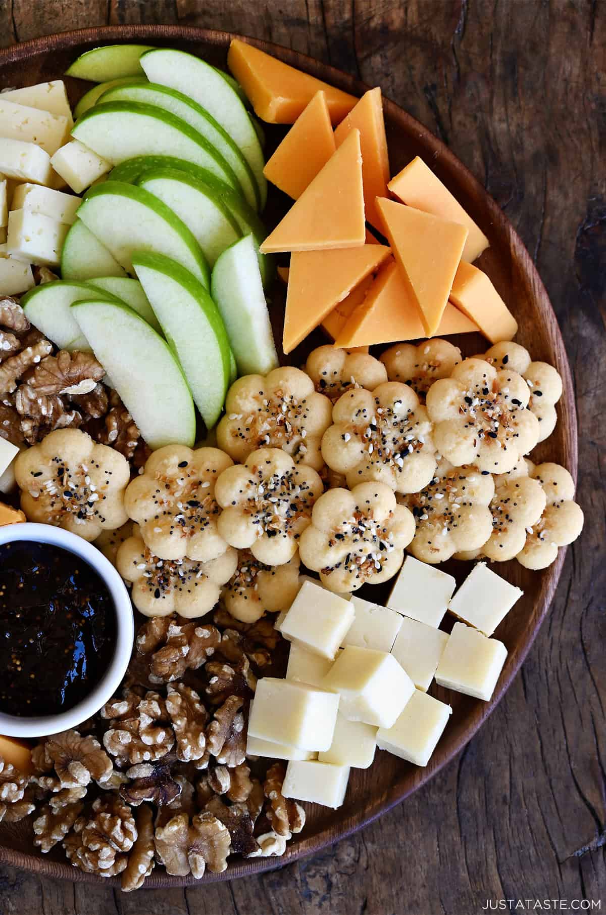 Homemade cheese crackers on a charcuterie board with meats, cheeses, walnuts, pecans, sliced green apple and a small bowl filled with preserves.