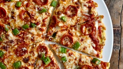 A hand grabs a slice of chicken crust pizza topped with diced green peppers and pepperoni cut into eight slices.