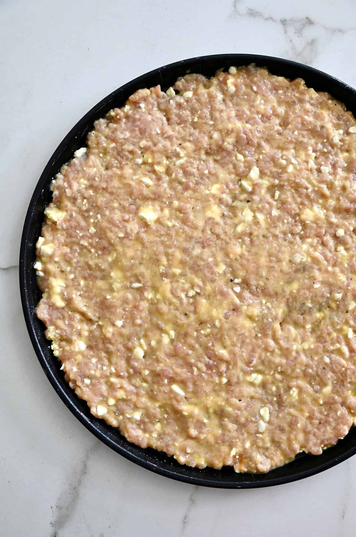 Shaped chicken crust on a pizza pan before being baked.