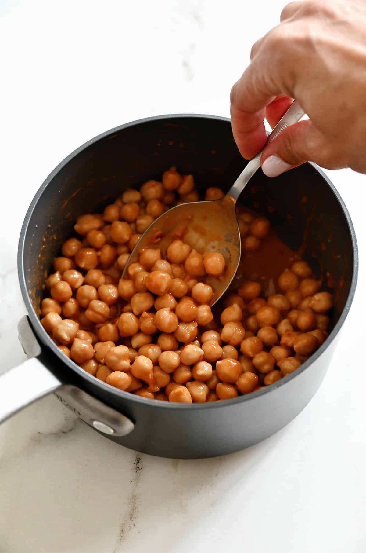 Chickpeas in a saucepan being tossed in Thai peanut sauce.