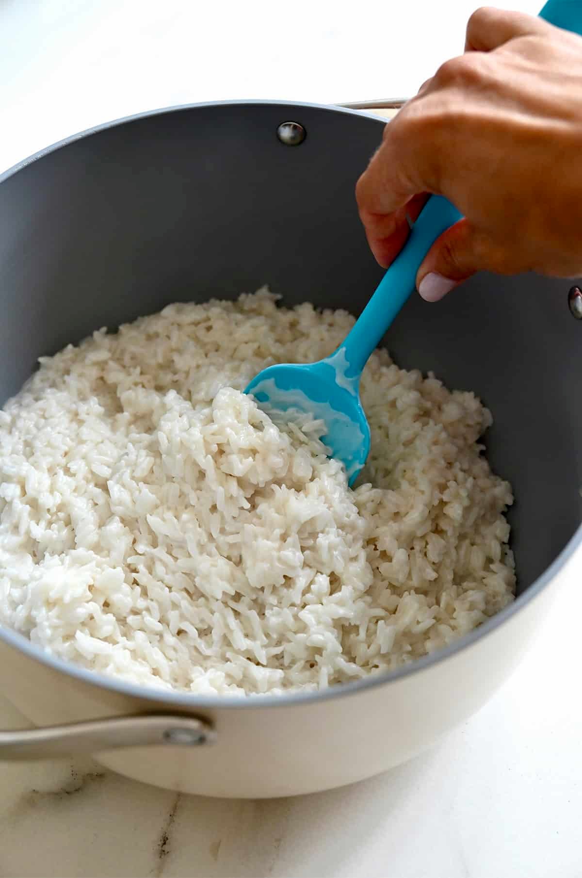 Fluffy coconut rice in a saucepan with a blue spatula.