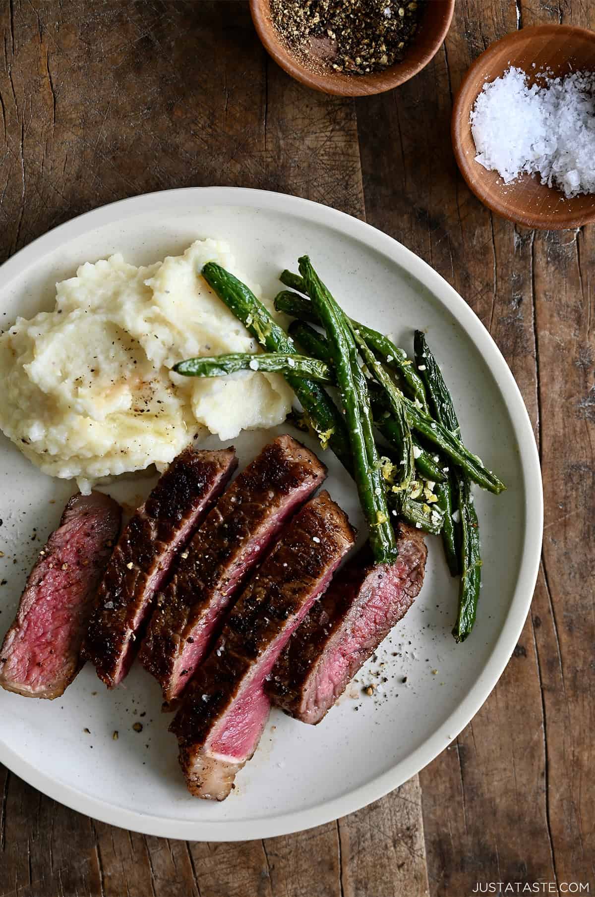 Sliced pan-seared steak served on a plate with blistered green beans and creamy mashed potatoes, showing a juicy pink center and golden crust.