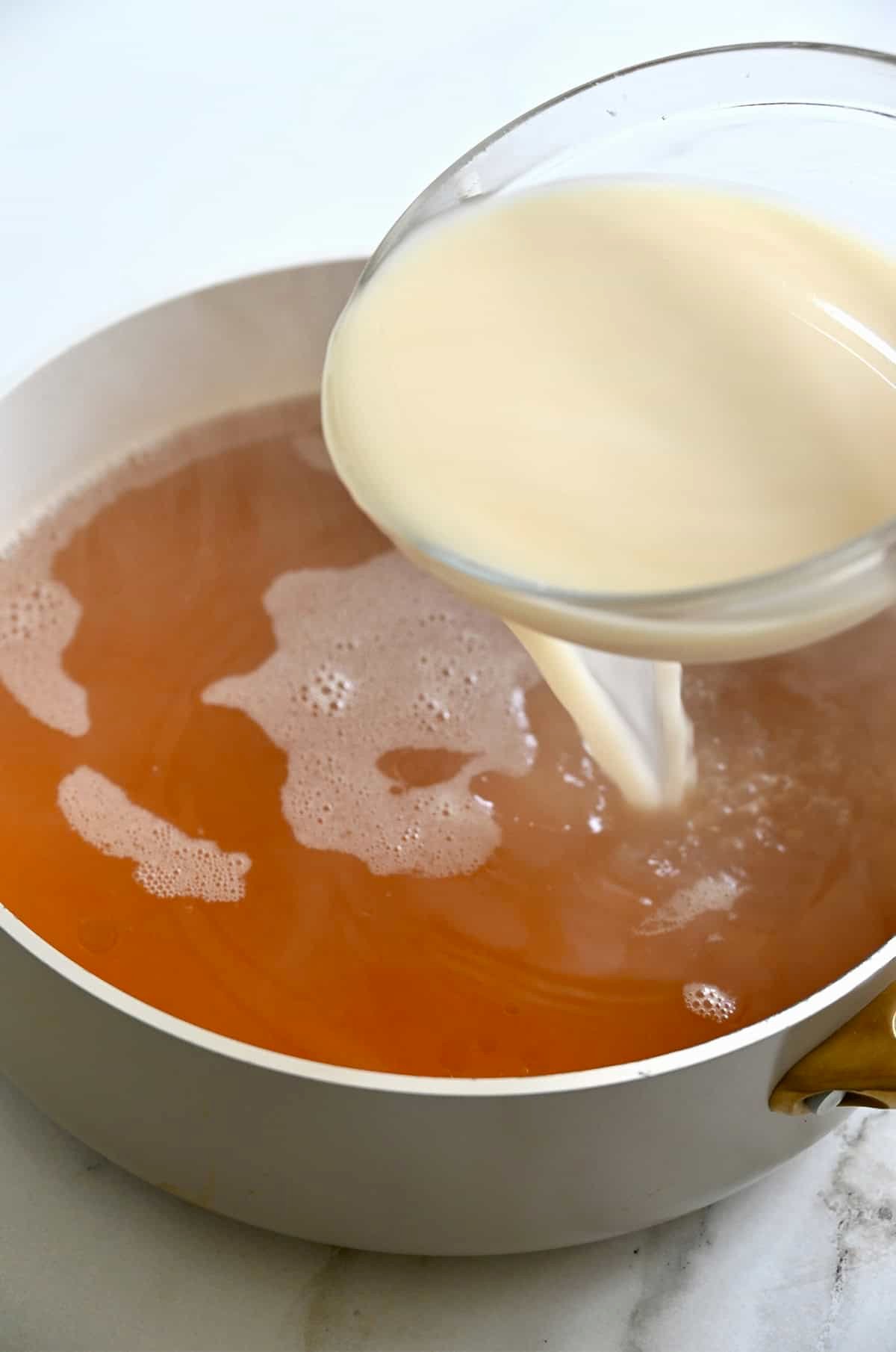 Adding a cornstarch slurry into a stock pot containing broth for egg drop soup.