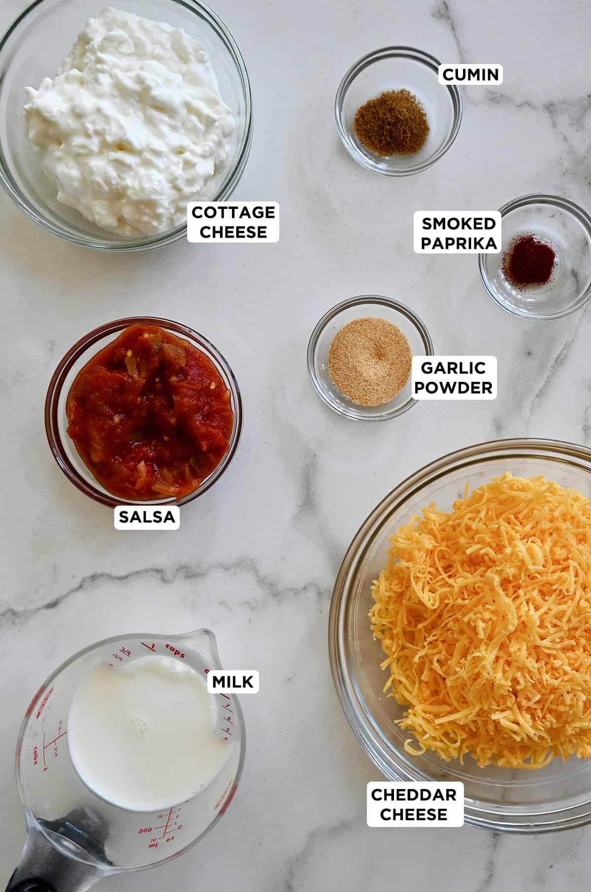 Ingredients to make the viral TikTok cottage cheese queso dip, including salsa, cottage cheese, shredded cheddar, milk, garlic powder, smoked paprika and cumin.