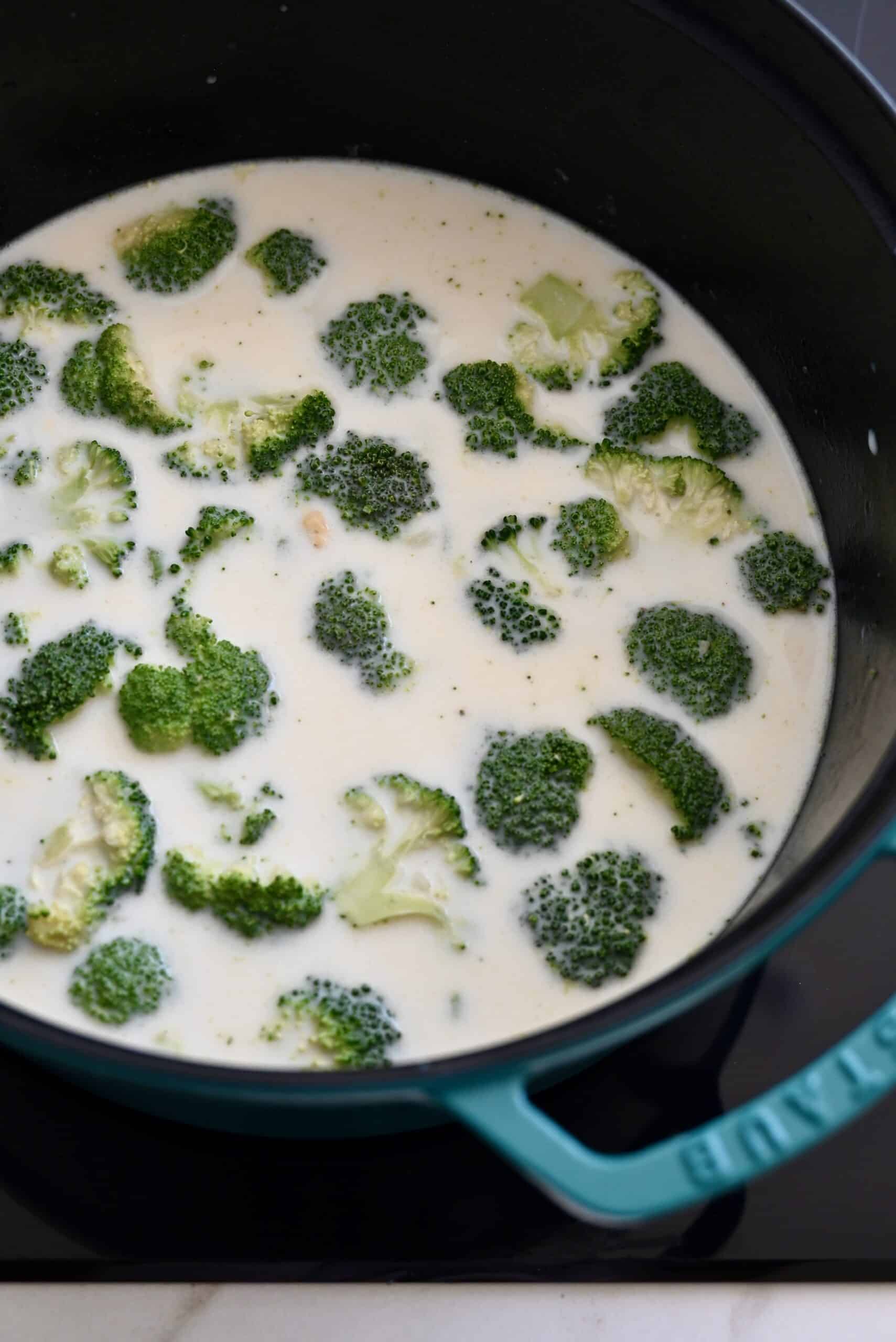 Broccoli florets simmering in milk and chicken stock in a stockpot.