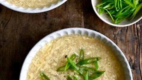 Two bowls of homemade egg drop soup topped with chopped scallions.