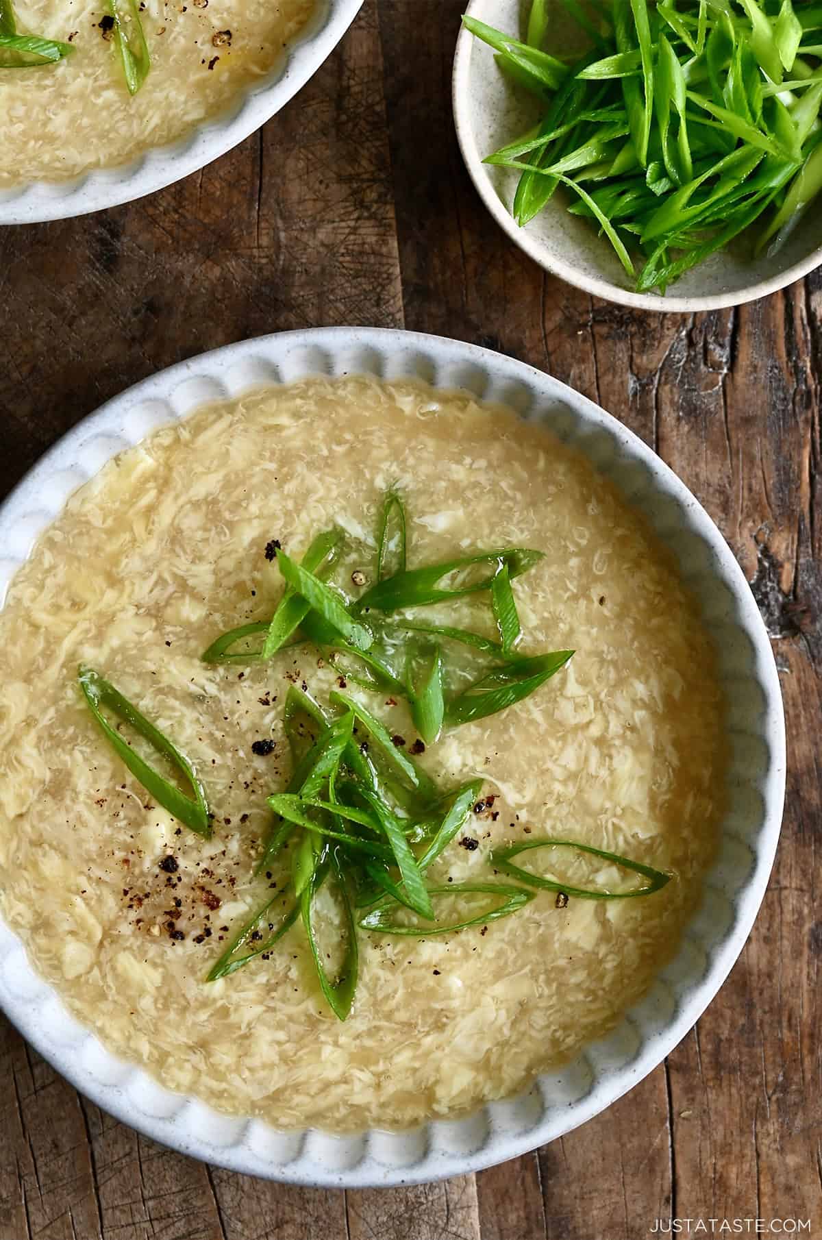 A bowl of homemade egg drop soup topped with thinly sliced scallions, showing silky ribbons of cooked egg in a golden broth.