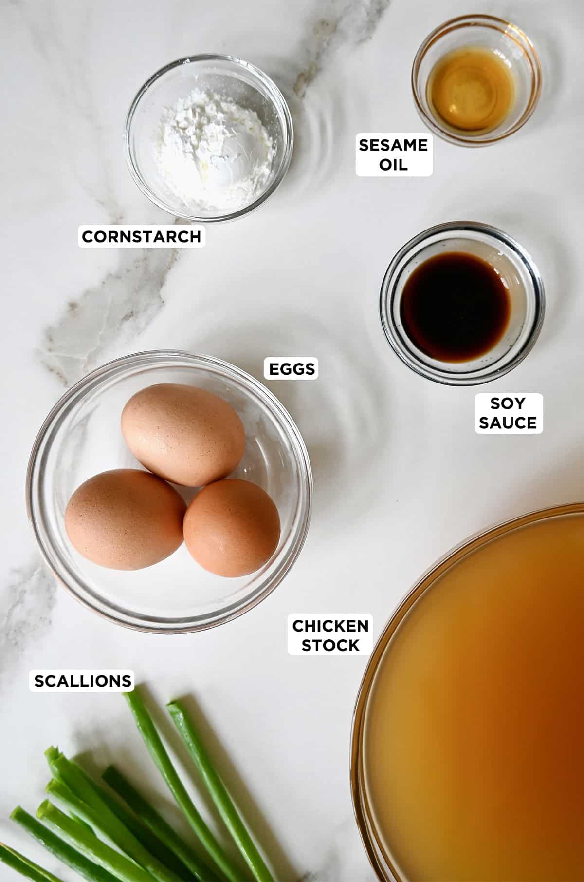 Ingredients to make egg drop soup, including chicken stock, eggs, soy sauce, sesame oil and cornstarch.