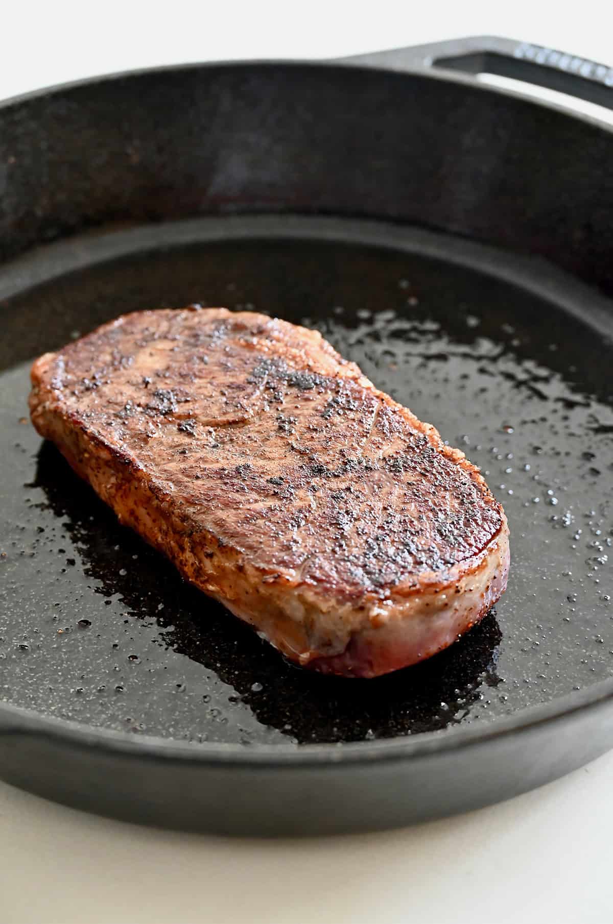 Searing the second side of a steak after flipping it in a hot cast-iron pan.