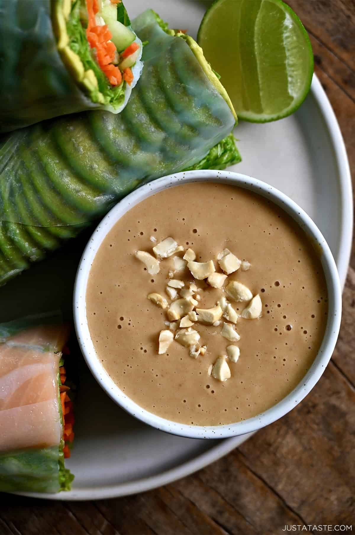 A bowl containing homemade Thai peanut sauce garnished with chopped peanuts on a plate with fresh spring rolls.
