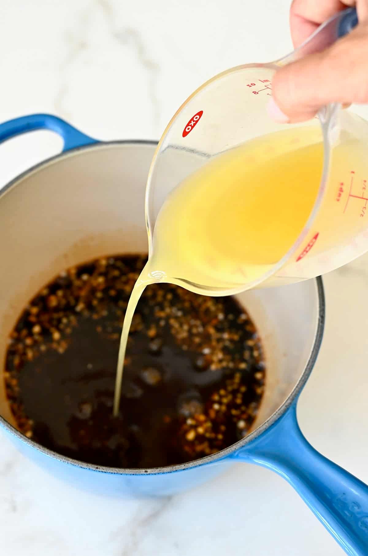 Pouring pineapple juice into a saucepan containing soy sauce, brown sugar, garlic and ginger.