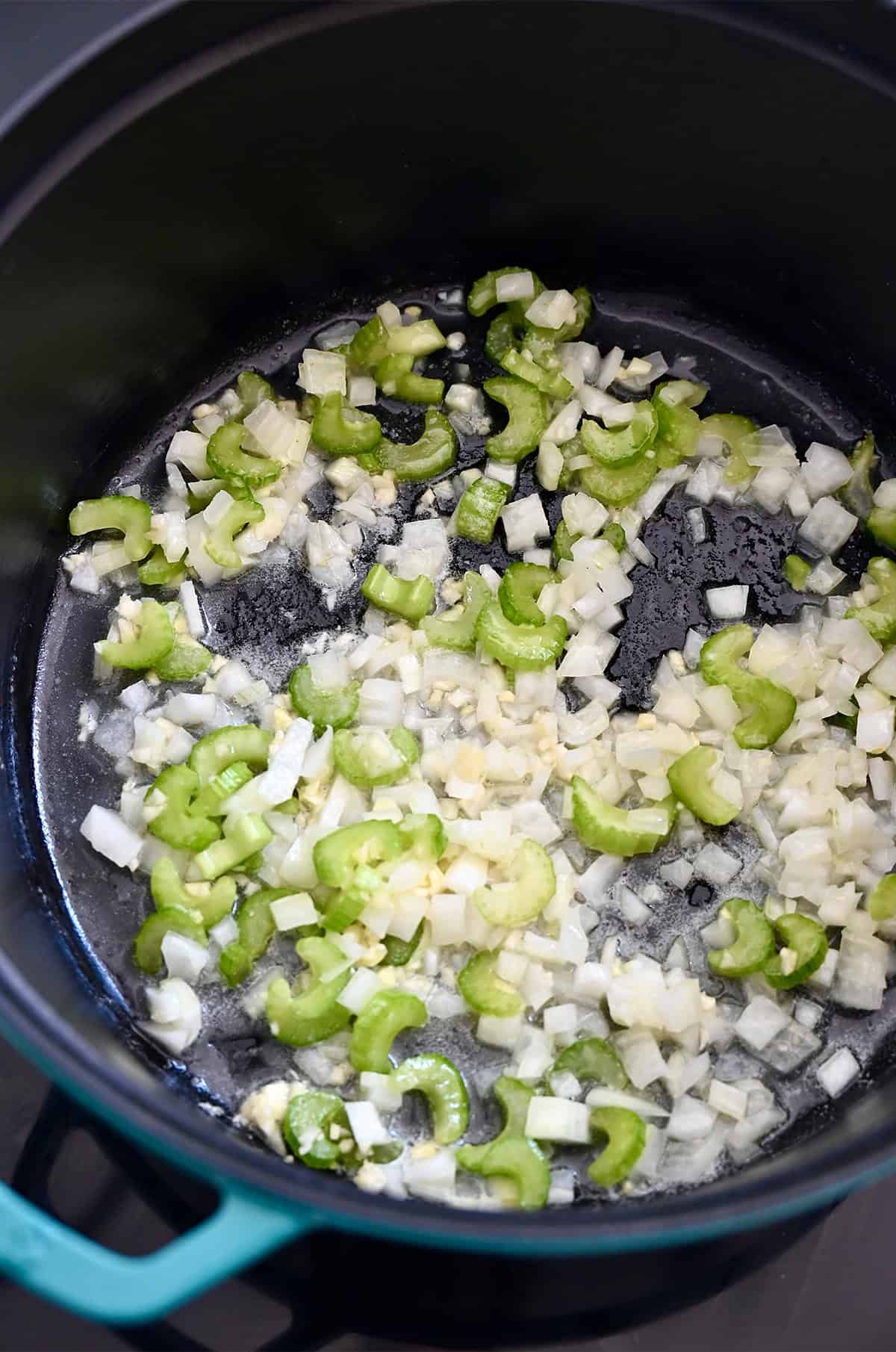 Onions, celery and garlic sautéing in melted butter in a large stockpot, the first step in making homemade broccoli cheddar soup.