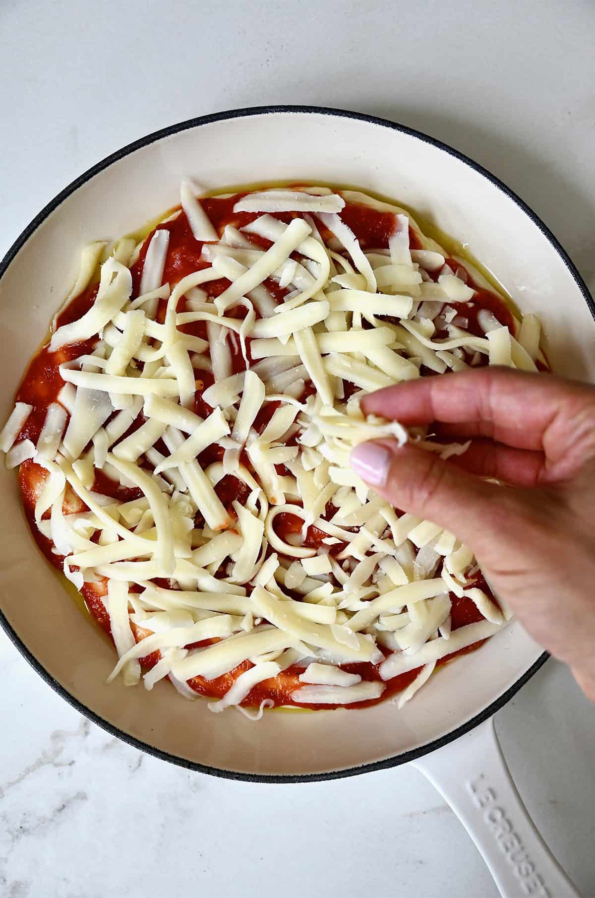 Adding shredded mozzarella cheese to pan pizza dough topped with marinara sauce.