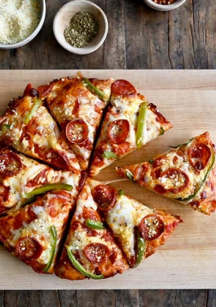 Cast iron pizza with pepperoni, green peppers, and plenty of cheese, cut into eight slices on a wooden cutting board.