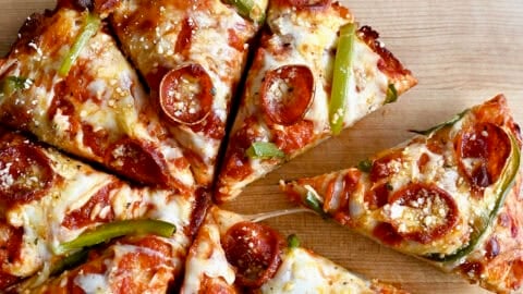 Cast iron pizza with pepperoni, green peppers, and plenty of cheese, cut into eight slices on a wooden cutting board.