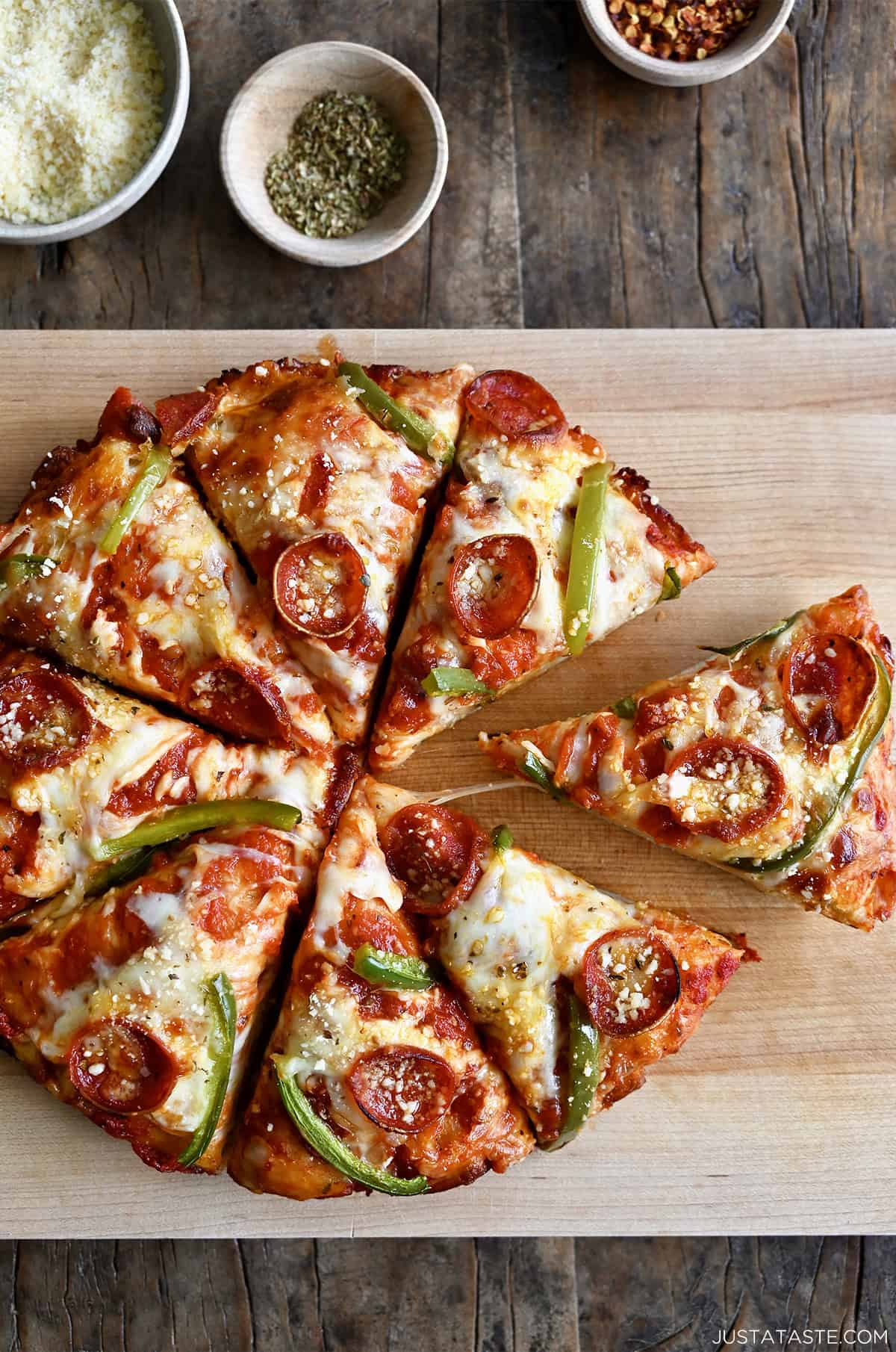 Cast iron pizza with pepperoni, green peppers, and plenty of cheese, cut into eight slices on a wooden cutting board.