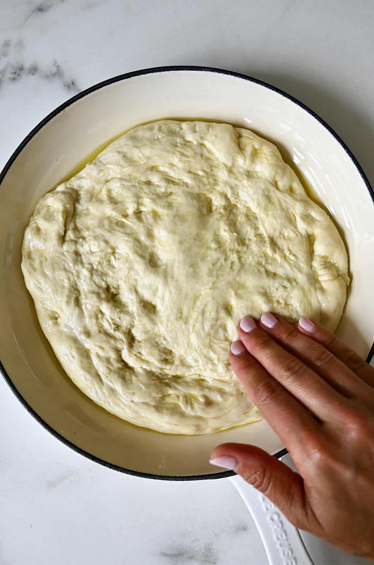 Pizza dough ball in a skillet with olive oil being turned once to coat, then pressed out to the edges. 