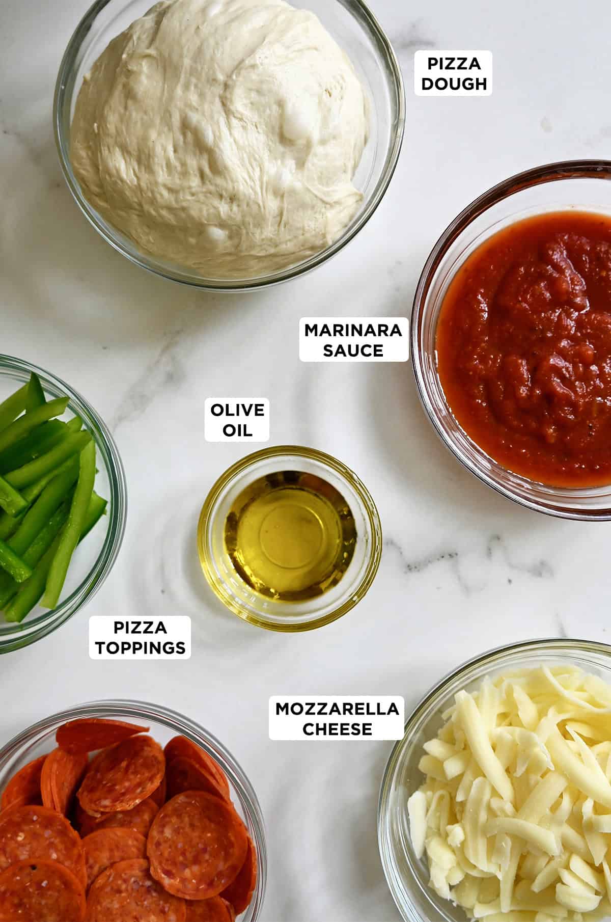 Pan pizza ingredients in glass bowls, including pizza dough, marinara sauce, shredded mozzarella cheese, pepperoni, and sliced green peppers.
