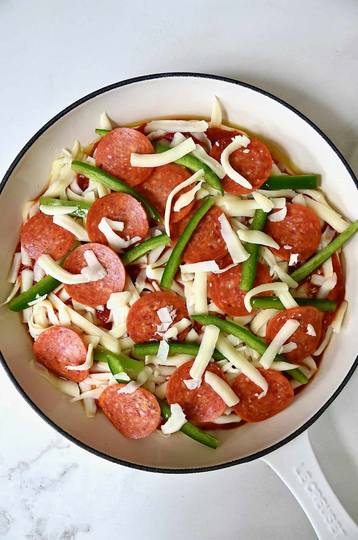 Adding pizza toppings (pepperoni and sliced green peppers) atop an unbaked pan pizza.