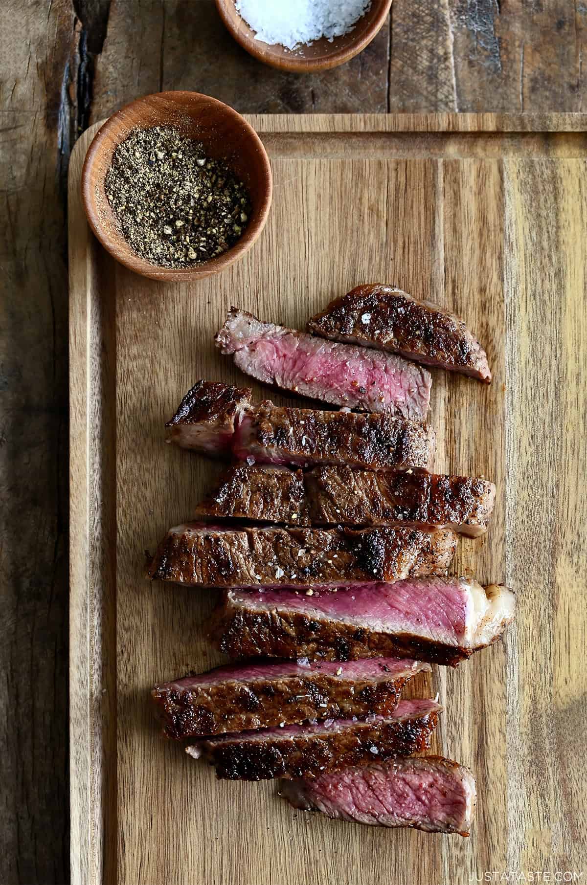 Sliced pan-seared steak on a cutting board, showing a juicy pink center and golden-brown crust.