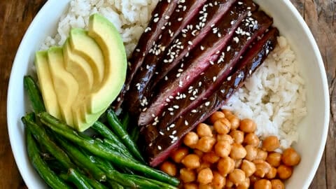 Beef teriyaki bowl with thin slices of steak, coconut rice, Chinese green beans, avocado and chickpeas tossed in peanut sauce.