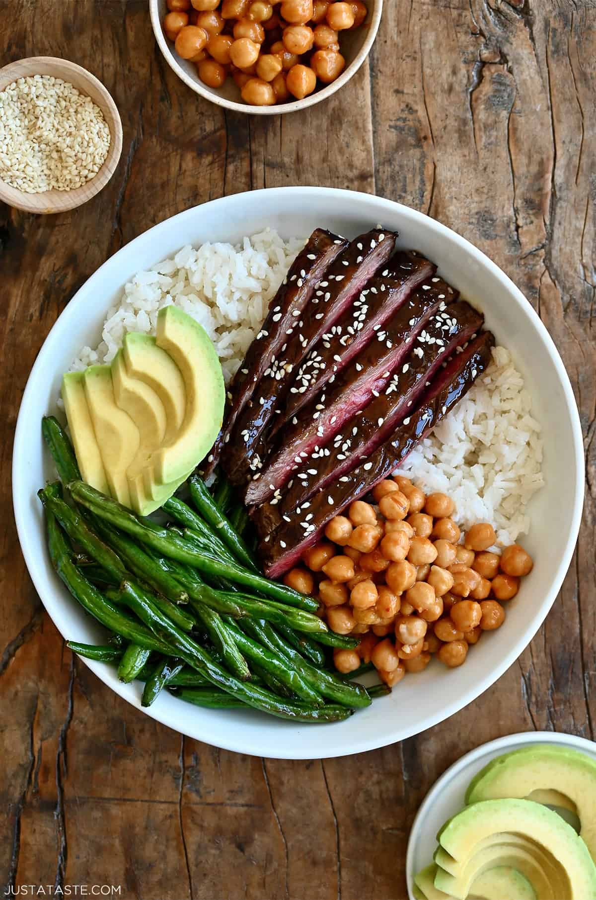 Beef teriyaki bowl with thin slices of steak, coconut rice, Chinese green beans, avocado and chickpeas tossed in peanut sauce.